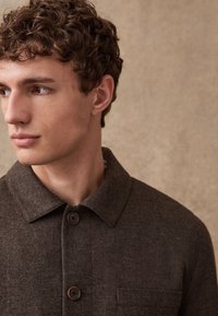 Brown wool blend jacket featuring a pointed collar, two front buttons, and a chest pocket, with a textured fabric and tailored fit.