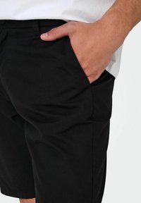Sorte shorts med en glat tekstur, der har en sidelomme og en afslappet pasform. Båret med en ensfarvet hvid top.