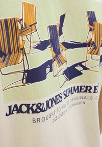 T-shirt featuring a graphic of five striped folding chairs in yellow and navy on a light green background, with text below.
