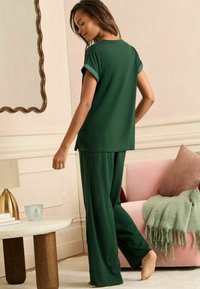 Conjunto de ropa de lounge verde que incluye una camiseta de manga corta y pantalones holgados. Tela suave, diseño relajado, que presenta puños de mangas enrollados.