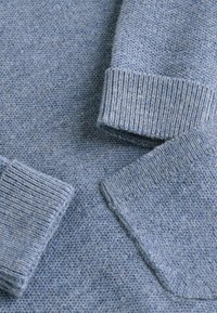 Hellblauer Strickpullover mit einem strukturierten Muster und gerippten Bündchen. Der Stoff hat ein weiches, leicht fusseliges Erscheinungsbild.