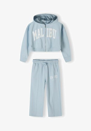 Sweatshirt court zippé bleu clair avec le texte "MALIBU" et un pantalon de jogging assorti présentant l'imprimé "USA 1967" en blanc. Tissu doux et coupe décontractée.