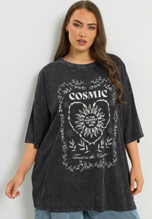 Frau trägt übergroßes schwarzes T-Shirt mit weißem Sonnen- und Blumendesign, Text "COSMIC" und "Trust in the Universe" auf der Vorderseite.