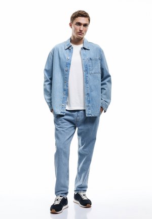 Lys blå denimskjorte med lomme, parret med matchende lys blå jeans. Stylet med sorte sneakers og en hvid T-shirt under.