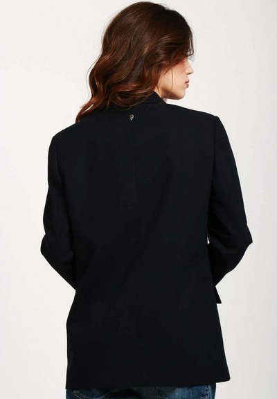 Blazer blu navy con una vestibilità dritta, spalle strutturate e maniche lunghe. Presenta un piccolo dettaglio metallico sullo scollo posteriore. Tessuto dalla consistenza liscia.