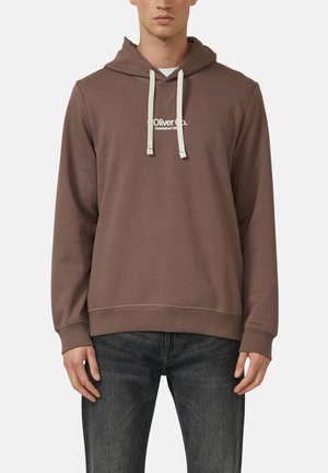 Mann trägt braunen Hoodie mit weißen Kordeln und dem Text „Oliver Co. Established 1901“, kombiniert mit schwarzen Jeans, steht vor weißem Hintergrund.