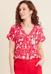 Blusa rossa a maniche corte con motivi grafici bianchi, dotata di scollatura a V e vestibilità rilassata, abbinata a pantaloni rossi coordinati.