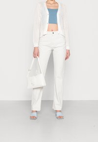 Un cardigan en tricot blanc sur un crop top à rayures bleues, associé à un jean blancs taille haute. Les accessoires comprennent un sac à main blanc et des sandales bleu clair.