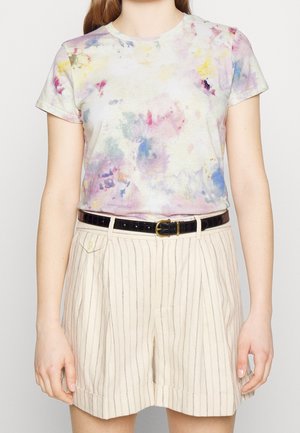 Osoba nosząca krótki rękaw koszulki tie-dye w pastelowych kolorach i beżowe spodenki w paski z czarnym paskiem.