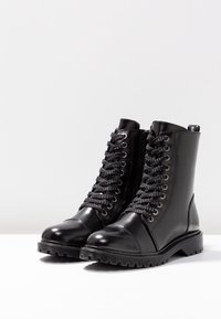 Par de botas de combate negras de cuero brillante con cordones, suelas de goma gruesa y cremalleras laterales sobre una superficie blanca.
