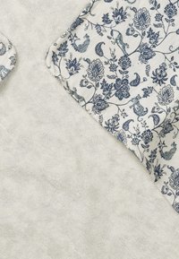 Valkoinen teksturoitu kangas, jossa on kerma- ja sinivärinen kukka- ja paisley-kuvioinen kangas, joka peittää osittain oikeaa yläkulmaa.