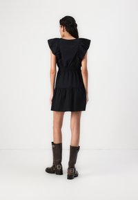 Vestido preto com mangas com folhos, cintura plissada e saia em camadas. Par de botins castanhos até ao joelho com fivelas. Design simples e contemporâneo.