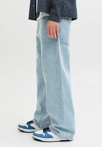 Világoskék laza szabású farmernadrág oldalzsebekkel és cipzáras sliccel, fehér és kék tornacipővel párosítva.