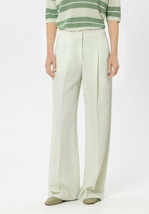 Loose-fitting, high-waist white trousers with front pleats, paired with olive green shoes and a green-and-white striped top.