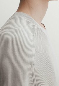 Pull en maille côtelée gris clair avec un motif texturé, présentant un col ras du cou et des manches montées, vu de côté.