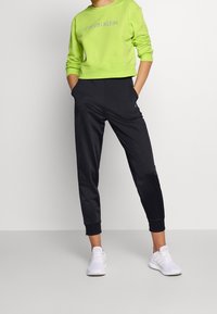 Jasnozielona bluza z logo "CALVIN KLEIN", zestawiona z czarnymi zwężanymi dresami. Białe buty sportowe dopełniają strój.