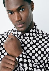 Camicia a bottoni bianca e nera con un design geometrico e motivi a pattern. Presenta un colletto e maniche lunghe con polsini abbottonati.