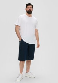T-shirt en coton blanc, coupe décontractée. Short bleu marine, longueur genou, tissu léger. Baskets blanches à lacets, design simple.