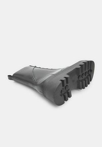 Stivale in pelle nera fino al polpaccio appoggiato di lato, che mostra una suola robusta con battistrada profondo e un tassello sul retro.