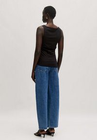 Schwarzes ärmelloses Oberteil mit rundem Ausschnitt, kombiniert mit weit geschnittenen blauen Jeans. Strukturierter Stoff, lässige Passform und schwarze High Heels.