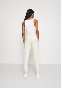 Joggers amarelos claros, ajustados, feitos de um tecido macio, com uma cintura elástica e bolsos laterais, combinados com ténis brancos.