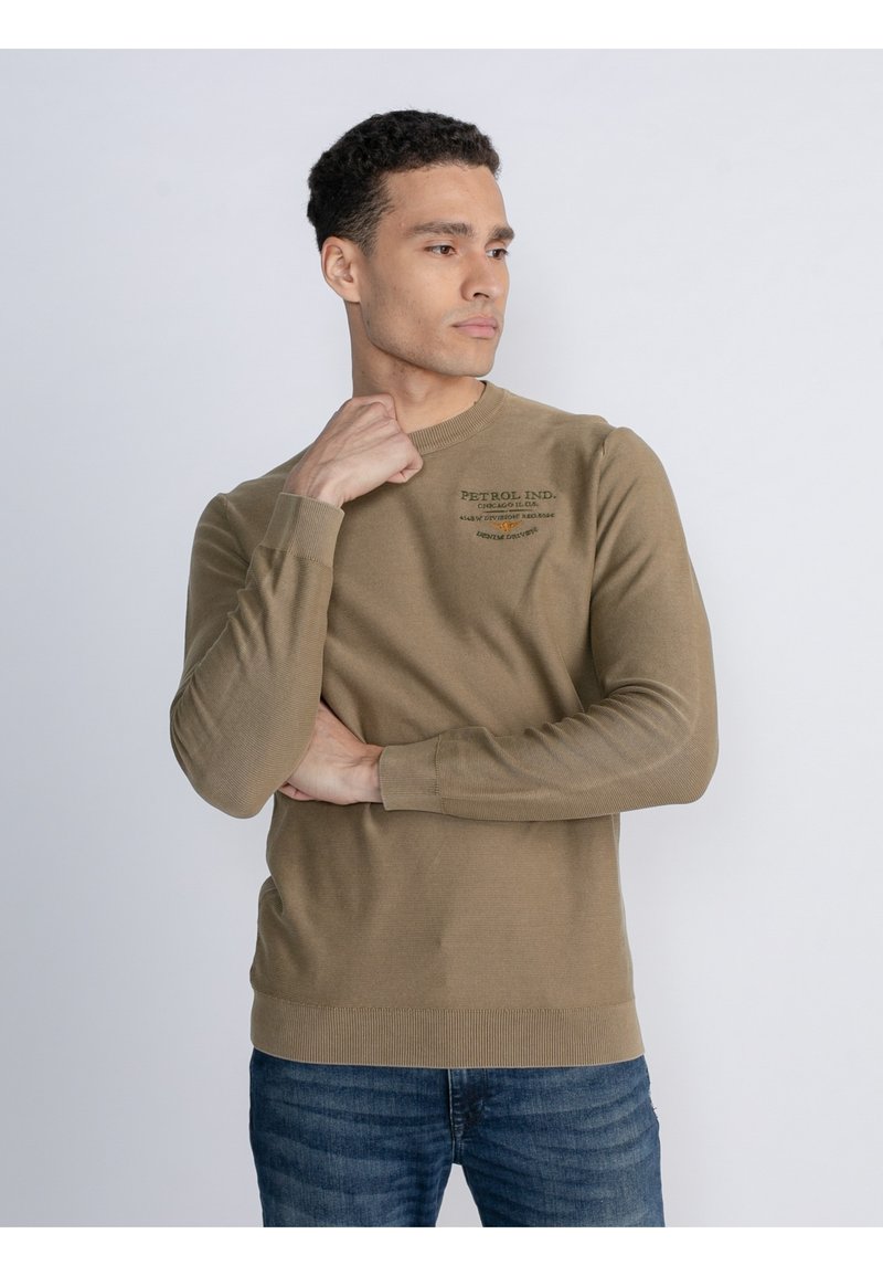Khakifarbener Langarm-Sweatshirt mit Rundhalsausschnitt und gerippten Bündchen und Saum, mit gedrucktem Logo-Detail auf der Brust. Kombiniert mit blauen Jeans.
