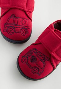 Röda tygbabyskor med marinblå sula, med broderade motiv av en ambulans och en brandbil på varje sko. Stängning med kardborreband.