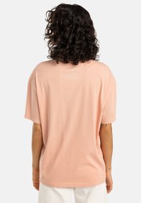 Lichtroze oversized katoenen t-shirt met korte mouwen en een ronde halslijn, met een gladde textuur en een relaxte pasvorm, gezien vanuit de achterkant.