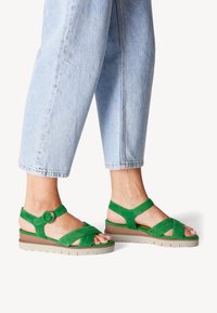 Sandali in suede verde con design a incrocio, accento in metallo circolare e leggera suola platform. Indossati con pantaloni cropped in denim chiaro.