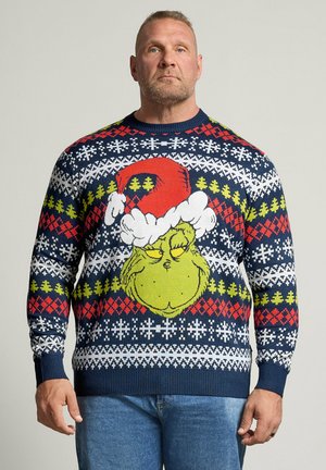 Hombre que lleva un jersey de Navidad azul con patrones rojos, blancos y verdes y una gran cara del Grinch con un gorro de Santa.