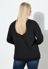 Sudadera negra de manga larga con cuello redondo, que presenta una textura suave y dobladillo acanalado, combinada con jeans azules.