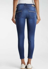 Smala jeans i mörkblå denim, med midja i normalhöjd, bakfickor och en slät yta. Stylar med vita texturerade skor.