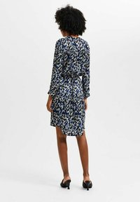 Sukienka w kwiatowy wzór w ciemnoniebieskim, kremowym i jasnoniebieskim kolorze, z długimi rękawami, talią podkreśloną paskiem oraz długością do kolan, o gładkiej teksturze.