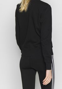 Zwarte sweatshirt van zachte stof met een ronde hals en geribbelde manchetten. Gecombineerd met zwarte legging met witte zijstrepen.