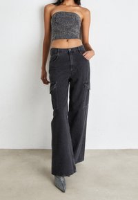 Svarta cargobyxor med vida ben, flera sidofickor och synlig sömnad. Bärs med en åtsittande strapless topp och spetsiga klackskor.