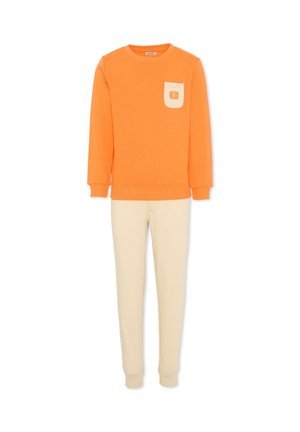 Pomarańczowa bluza z długim rękawem z kremową łatą na kieszeni, zestawiona z kremowymi zwężanymi spodenkami dresowymi na białym tle.