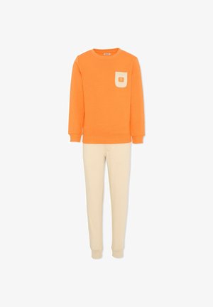 Pomarańczowa bluza z długim rękawem z kremową łatą na kieszeni, zestawiona z kremowymi zwężanymi spodenkami dresowymi na białym tle.