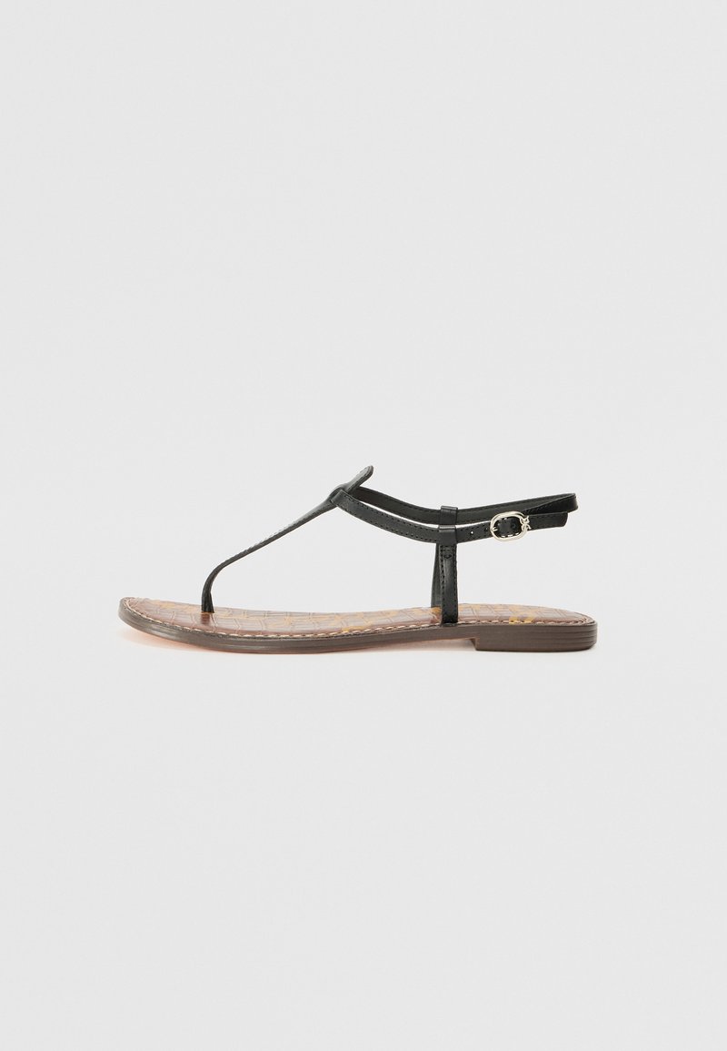 Μαύρες επίπεδες σανδάλια με σχέδιο T-strap, που διαθέτουν υφασμάτινη καφέ σόλα και πλαϊνό κούμπωμα για ρύθμιση.