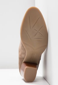 Bottine en daim marron à bout rond, dotée d'un petit talon en bois et d'une semelle en caoutchouc texturée avec des détails en forme de feuilles.