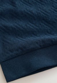 Dunkelblaues Sweatshirt mit einem strukturierten Zickzackmuster, geripptem Saum und weichem Stoff. Nahaufnahme, die die Handwerksdetails hervorhebt.