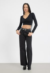 Svart, ribbestrikket langermet crop-top med frontruffles, parret med høyt liv svarte vide jeans og et naglet belte. Svart hælboots.