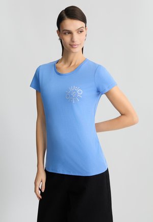 T-shirt di cotone blu con maniche corte e scollatura rotonda. Presenta una stampa del logo argentato sul petto. Texture liscia e forma aderente.
