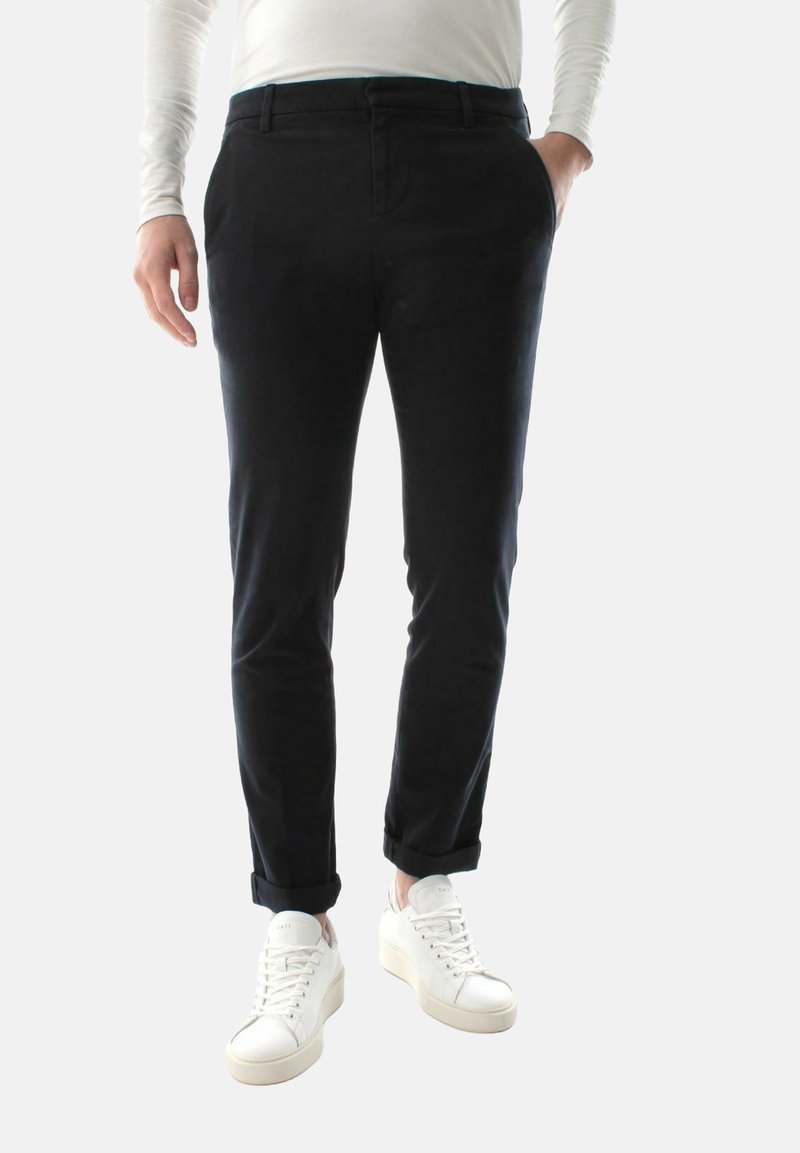 Sorte tapered bukser med en glat tekstur, der har en rullet kant ved anklen og bæres med hvide sneakers.