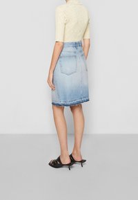 Denim kokerrok met een lichtblauwe ombre effect, rafelige zoom en twee achterzakken; gecombineerd met zwarte open hakken.