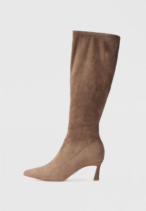 Bota castanha em camurça até ao joelho, com bico fino e salto afilado, apresentando uma textura suave e um design sem emendas.