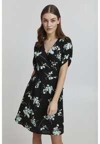 Blommig omlottklänning i svart tyg med mintgröna blomster mönster. Korta puffärmar och en V-ringning. A-linjeformad silhuett.