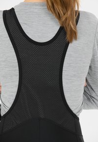 Nahaufnahme einer Person, die einen schwarzen Radträger mit Netzrücken über einem hellgrauen Langarmshirt trägt, mit Blick auf den oberen Rücken- und Schulterbereich.