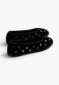 Zapatos planos de terciopelo negro con tachuelas circulares plateadas a lo largo del borde superior, con puntera redondeada y suela de goma texturizada.