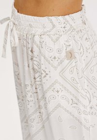 Kalhoty s elastickým pasem z lehkého materiálu, s potiskem bílé a šedé bandany, zavazováním v pase a malým logem na boku.