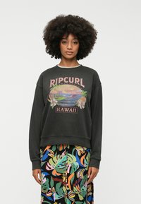 Sweatshirt noir avec un imprimé graphique au style vintage portant l'inscription "Ripcurl Hawaii". Associé à une jupe à motifs floraux multicolores.